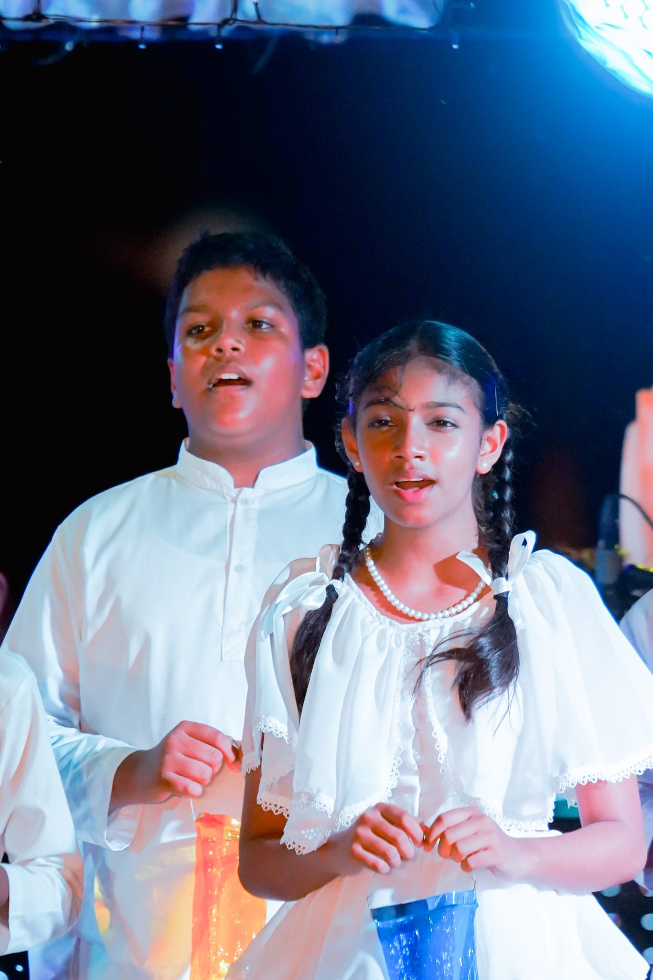 Children performing in traditional white attire during a ceremonial event.