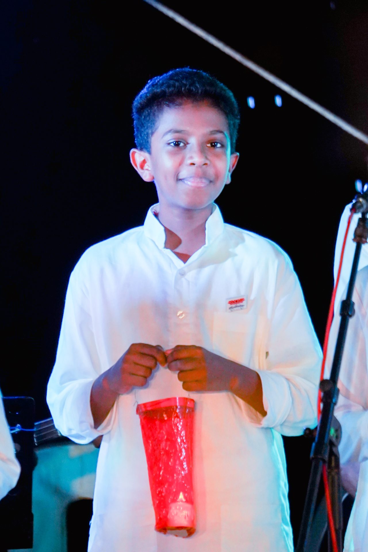Boy holding red lantern on stage in traditional white outfit.