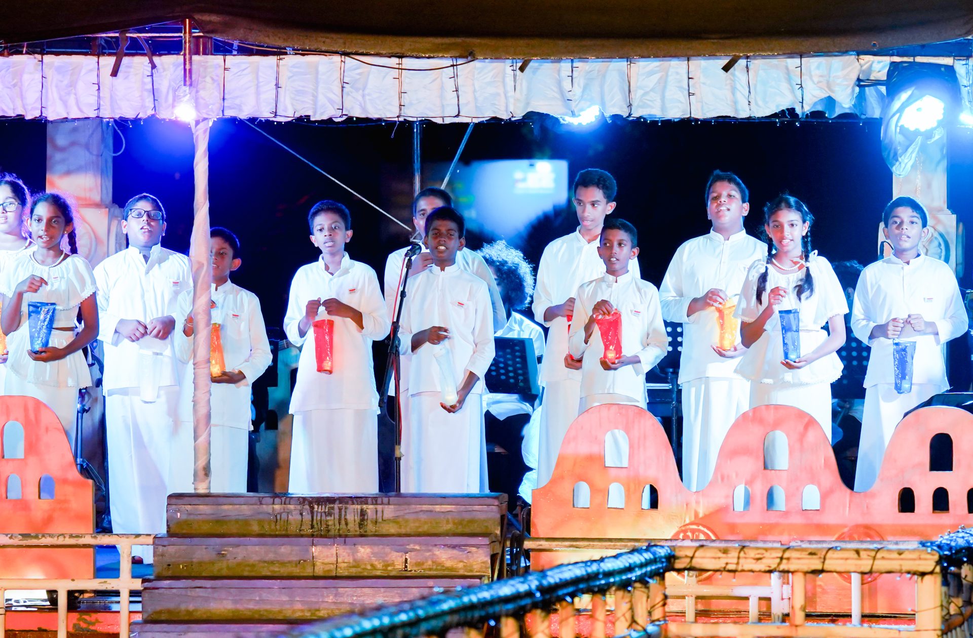 Youth performance on stage with lanterns, traditional white costumes, and colorful decorations.