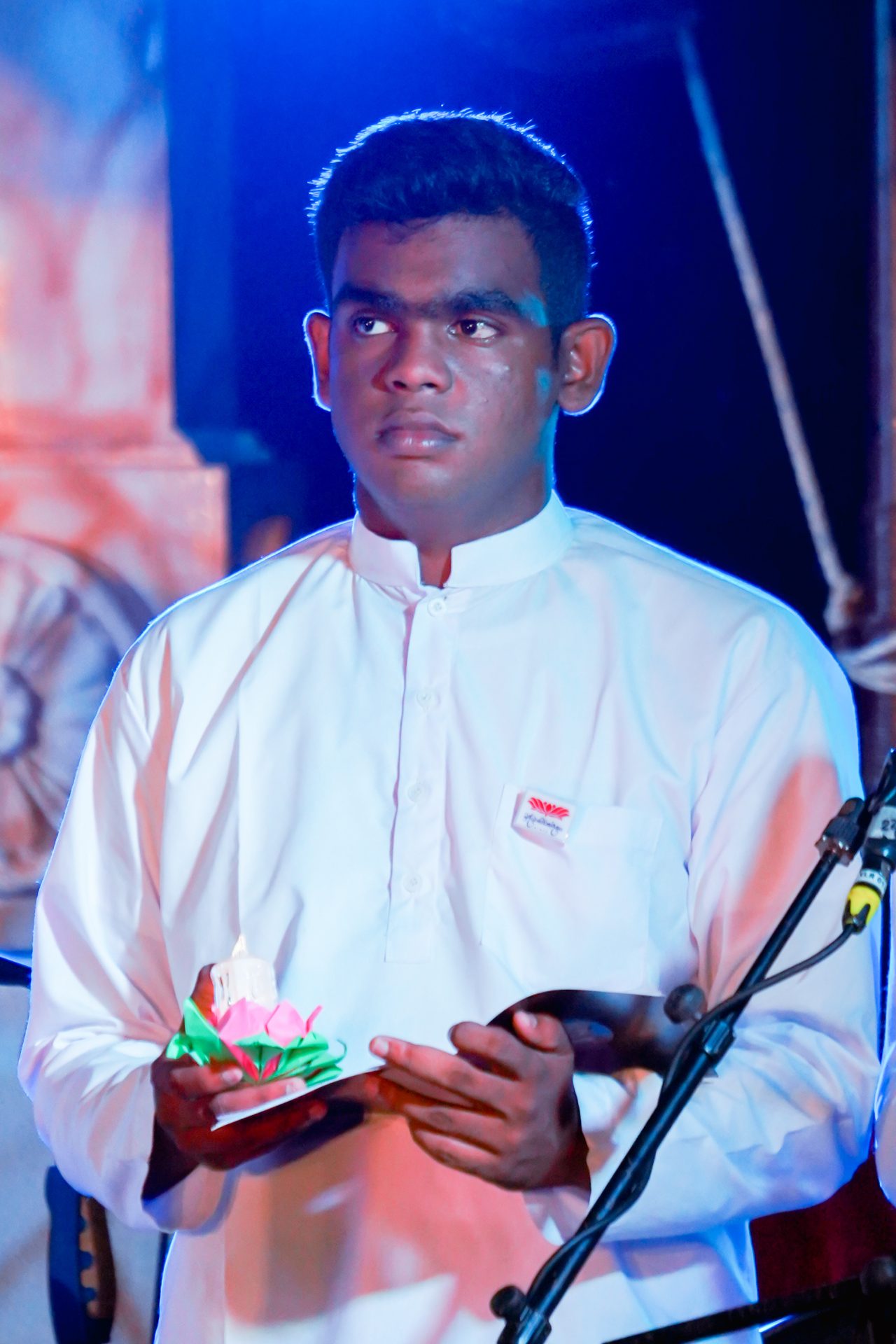 Young man holding decorative candle during solemn stage ceremony.