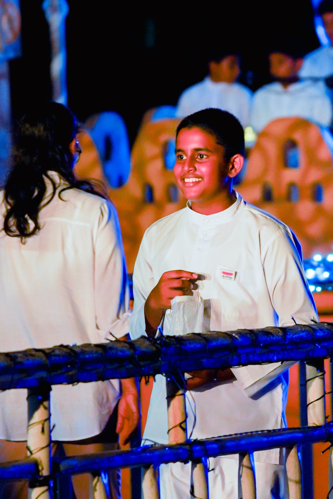 Young boy in traditional attire smiles at vibrant cultural festival.