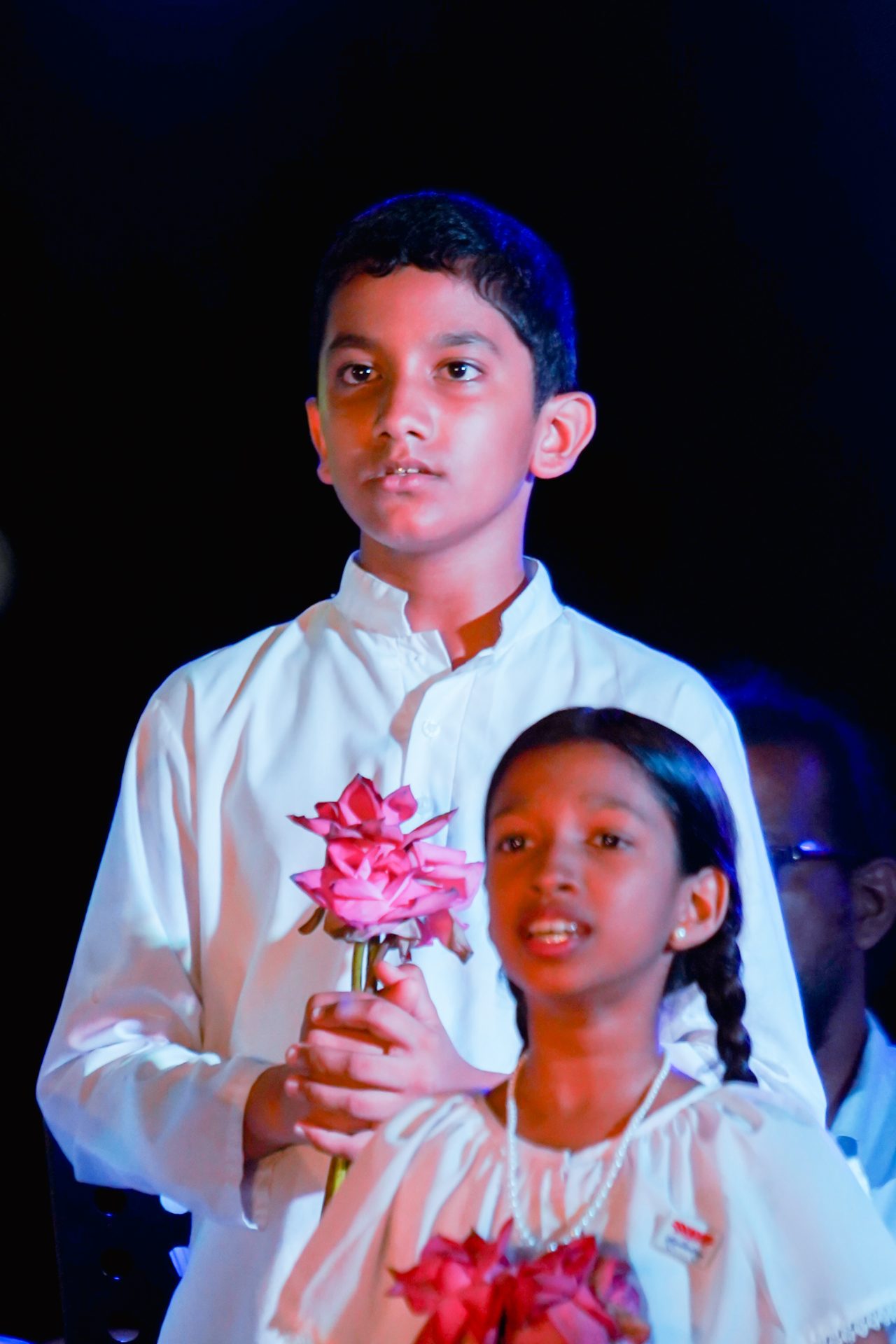 Children holding pink flowers at a ceremony.
