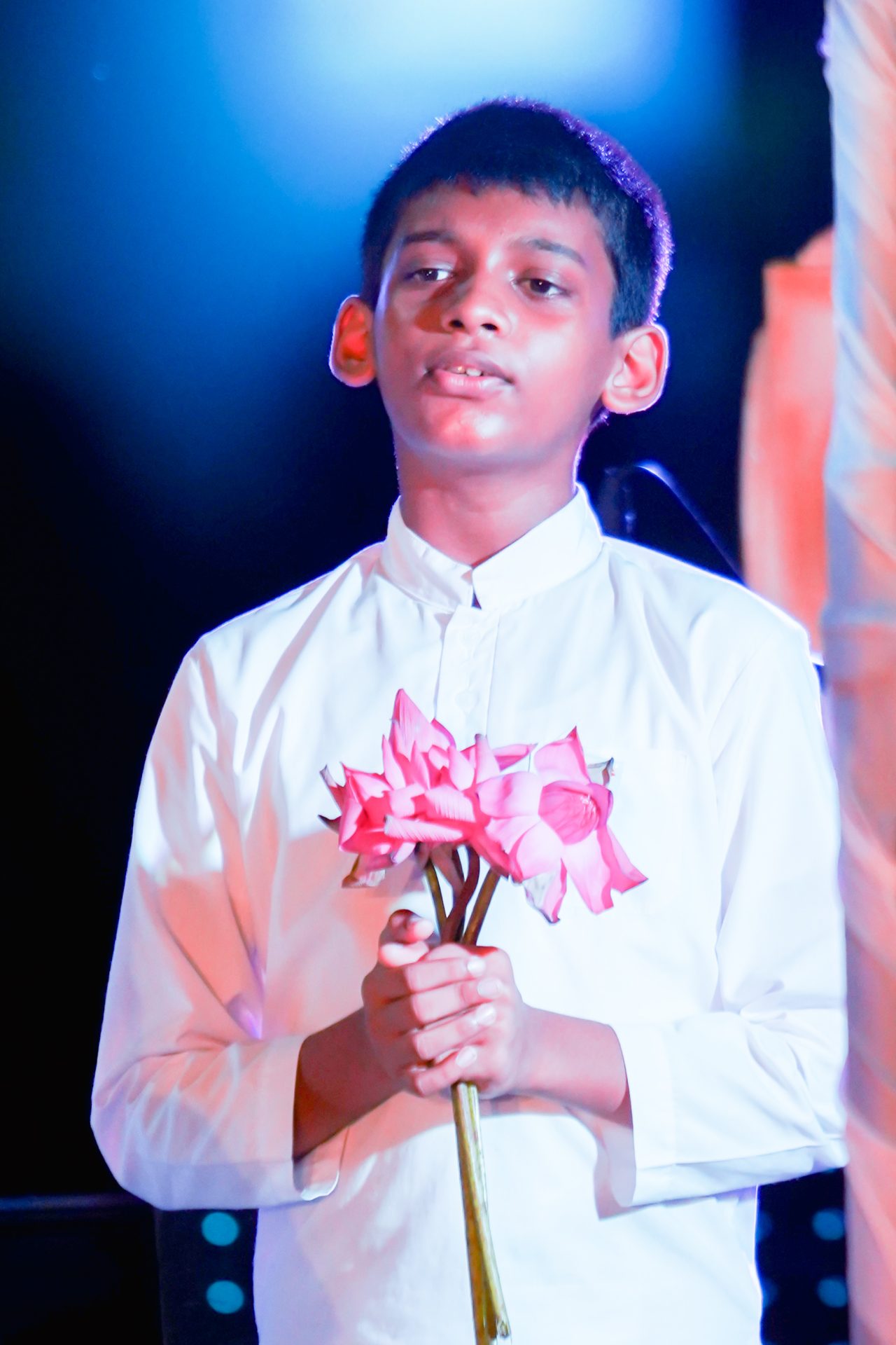Boy holding pink flowers on stage with halo effect.