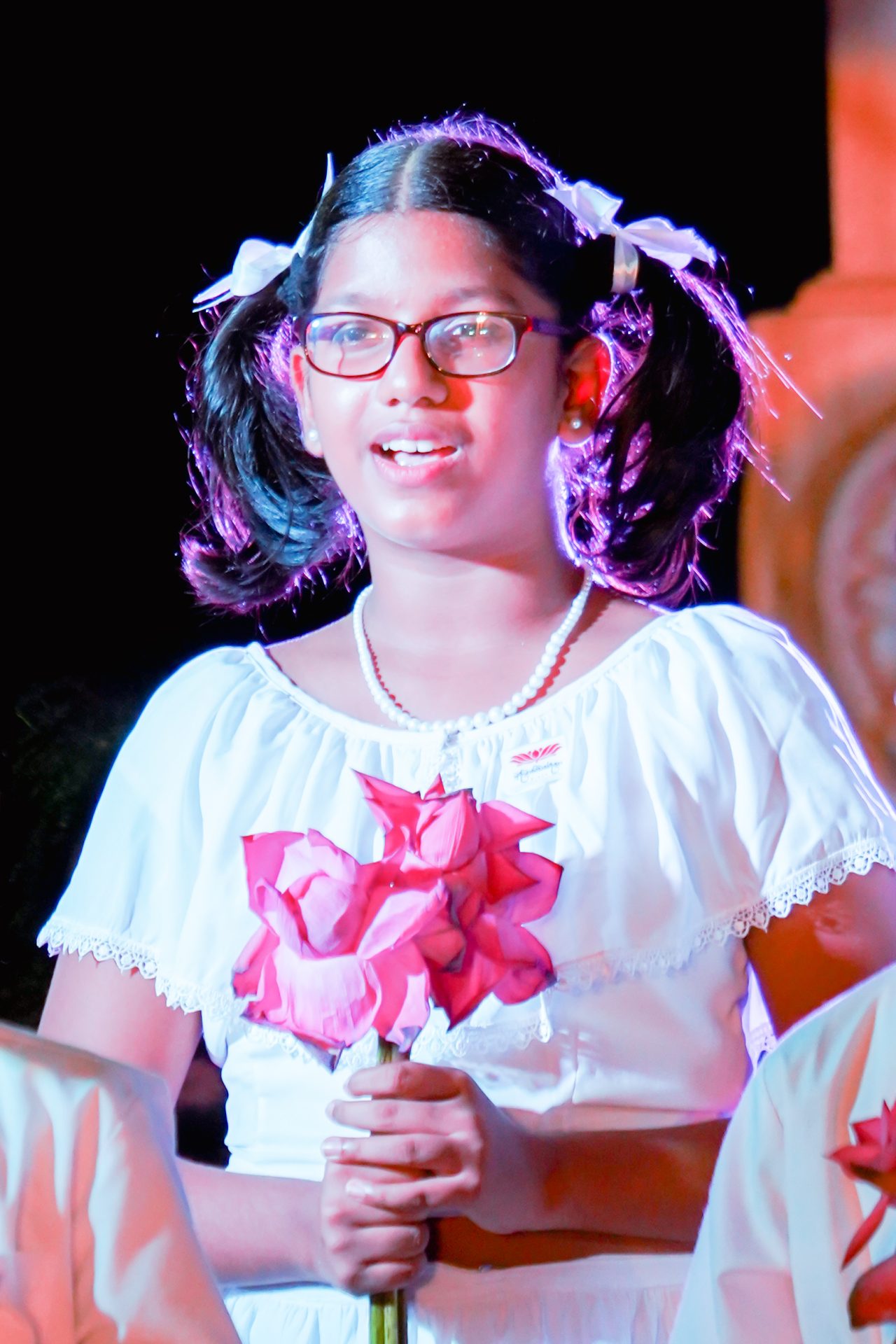 Young girl in white dress holding pink flowers at event.