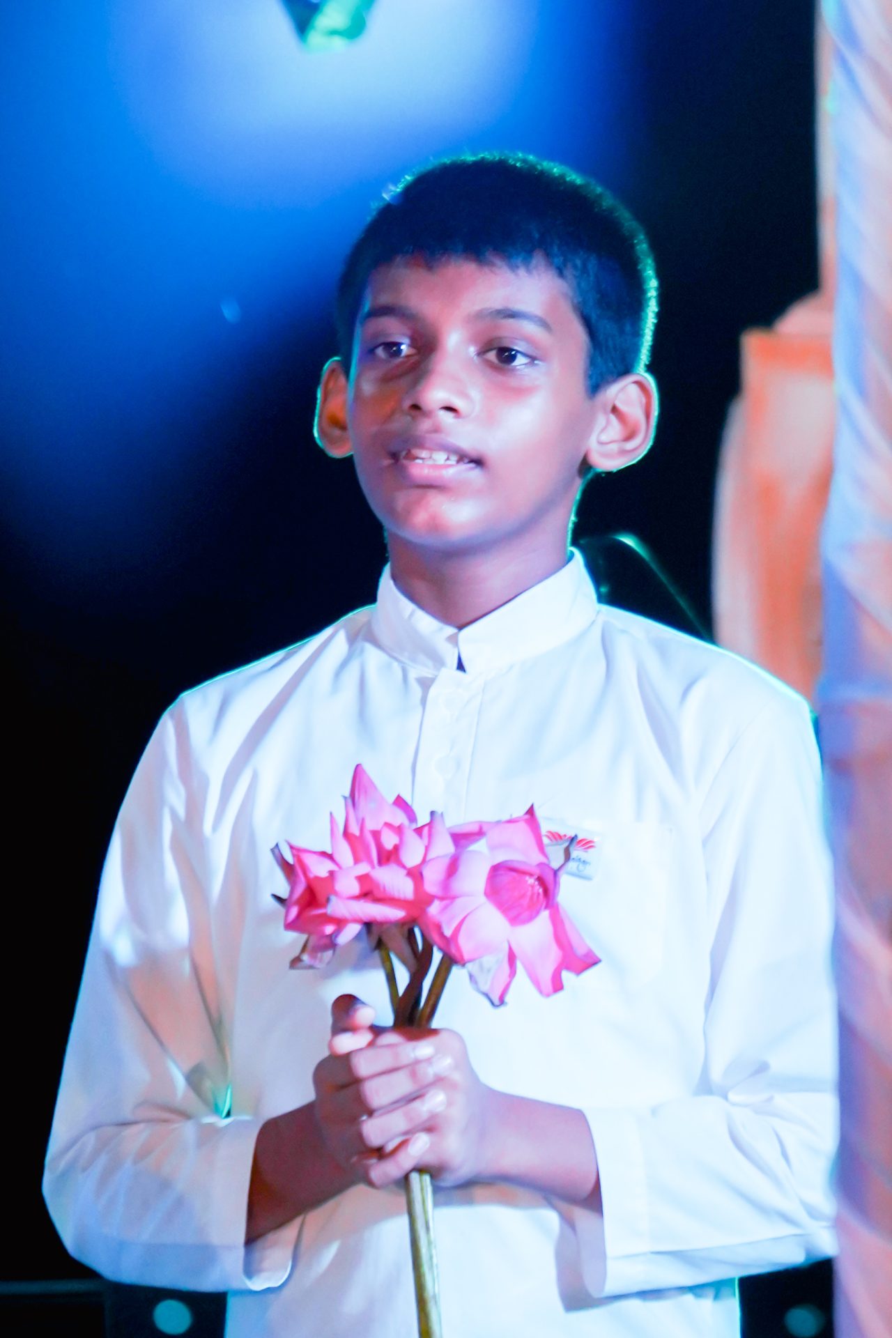 Boy holding pink lotus flowers in white shirt with blue background.