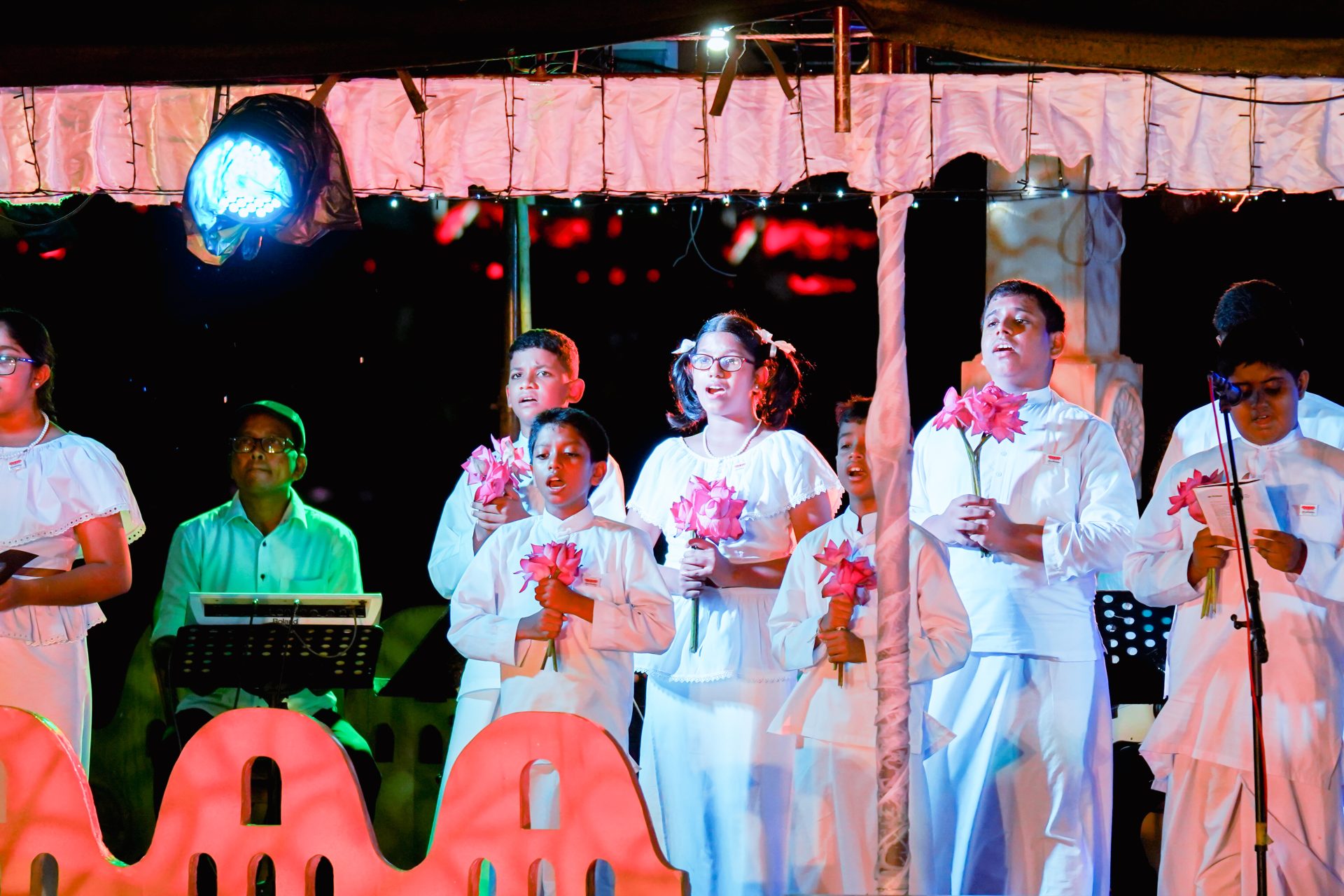 Childrens choir performing under festive canopy with lotus flowers.