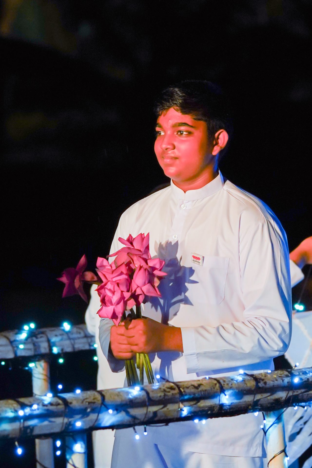 Young person in white holding pink flowers at night ceremony.