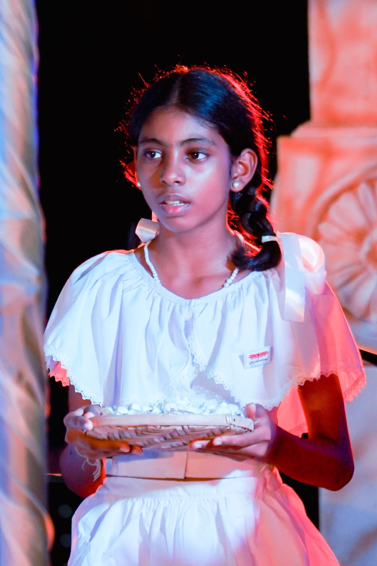 Young girl in white dress holding flower basket on stage.