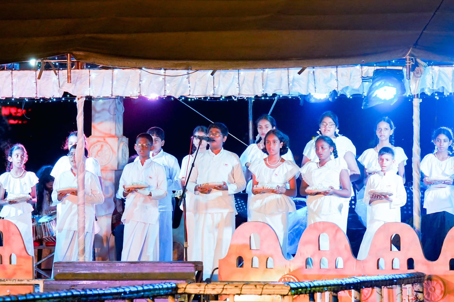 Children performing traditional ceremony on stage with offerings and decorations.