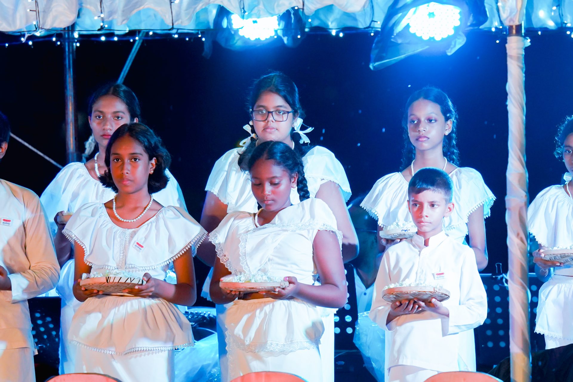 Children in white outfits at a blue-lit cultural ceremony.