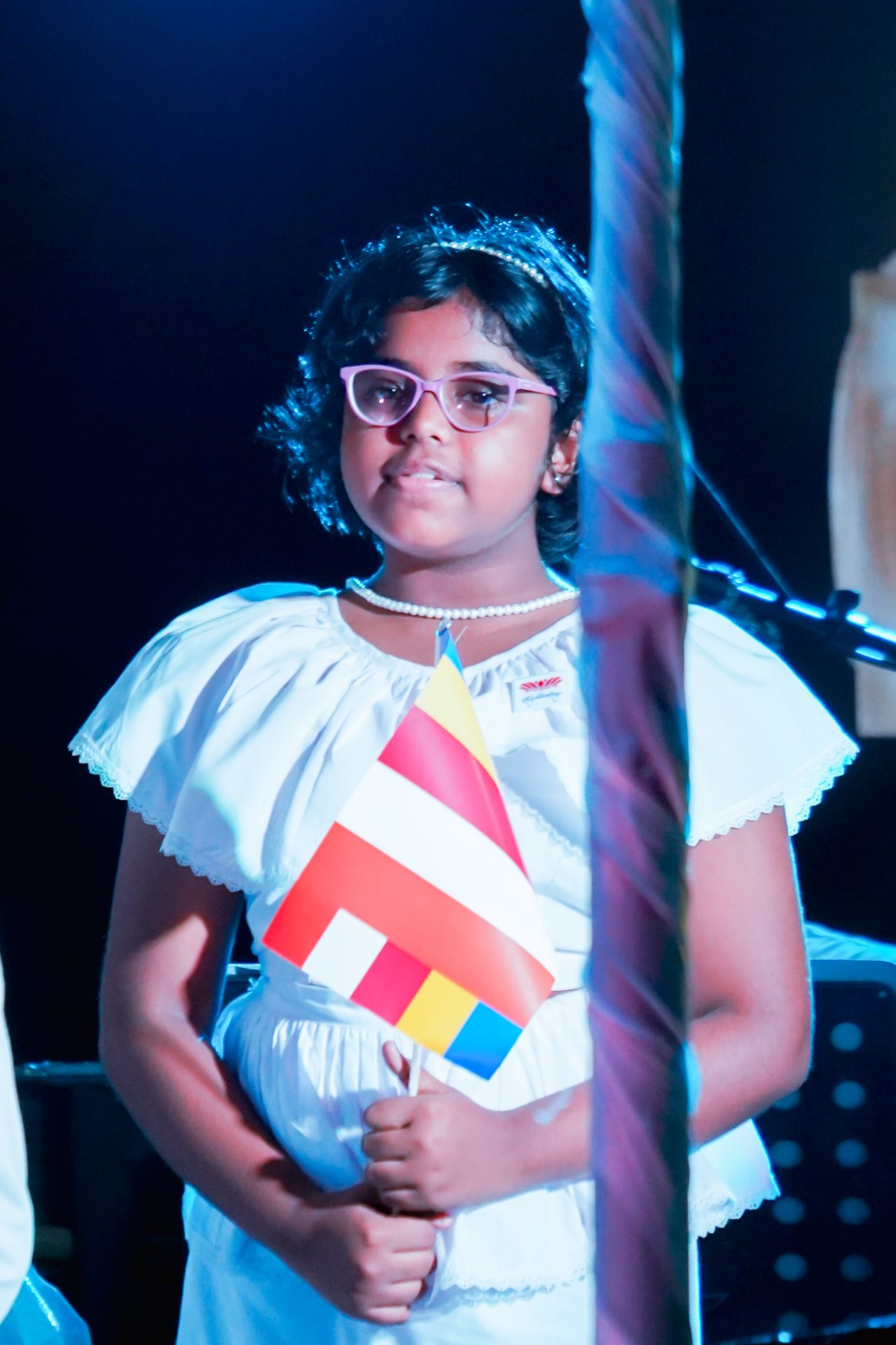 Young girl in white dress holding colorful flag at Buddhist ceremony.