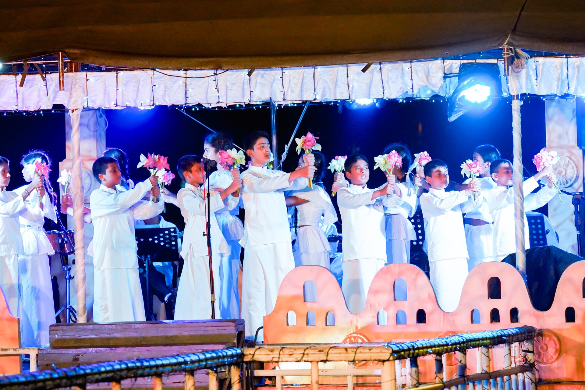 Childrens cultural performance with flowers on stage, traditional attire, evening ceremony.