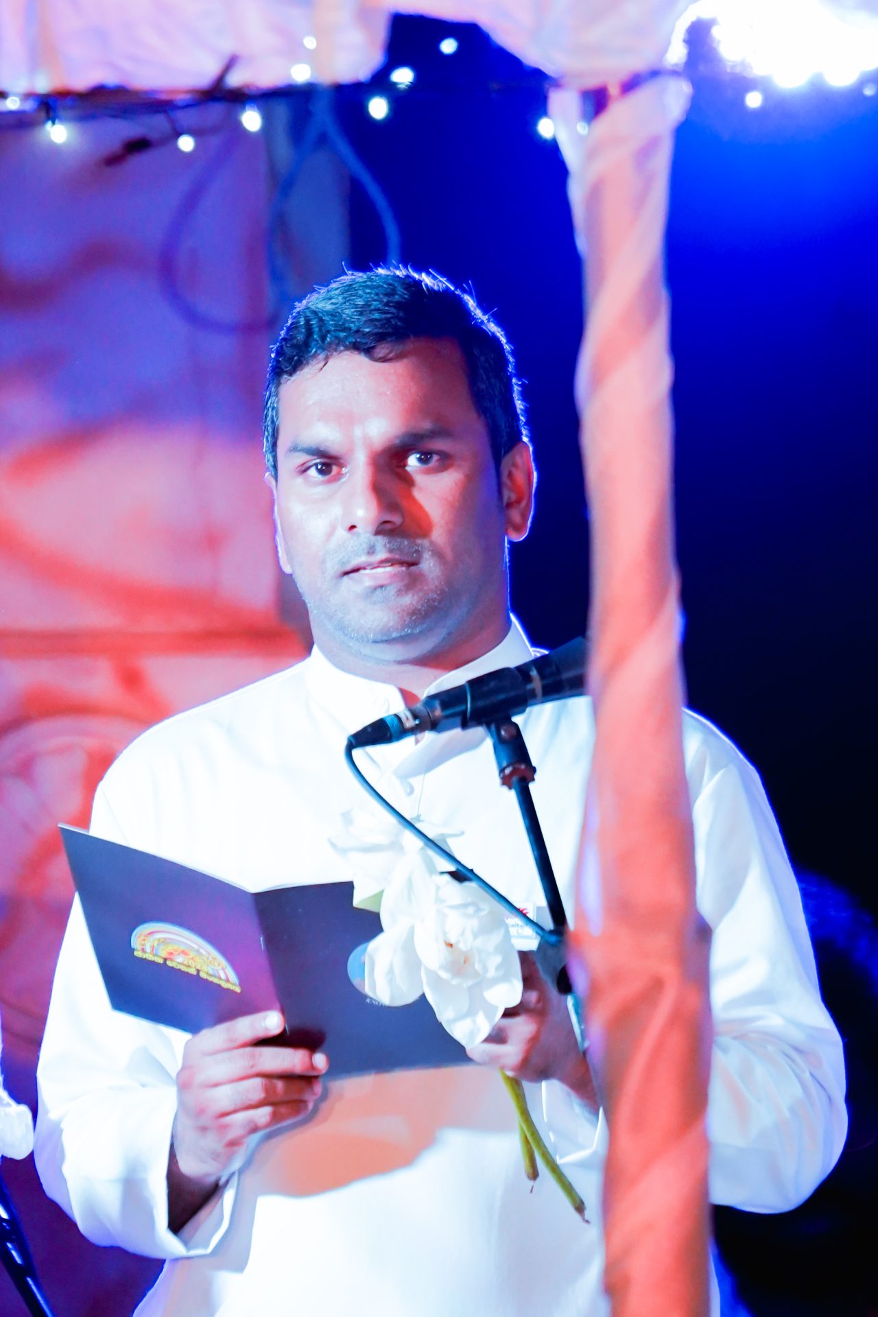 Man delivering speech at formal event with vibrant lighting.