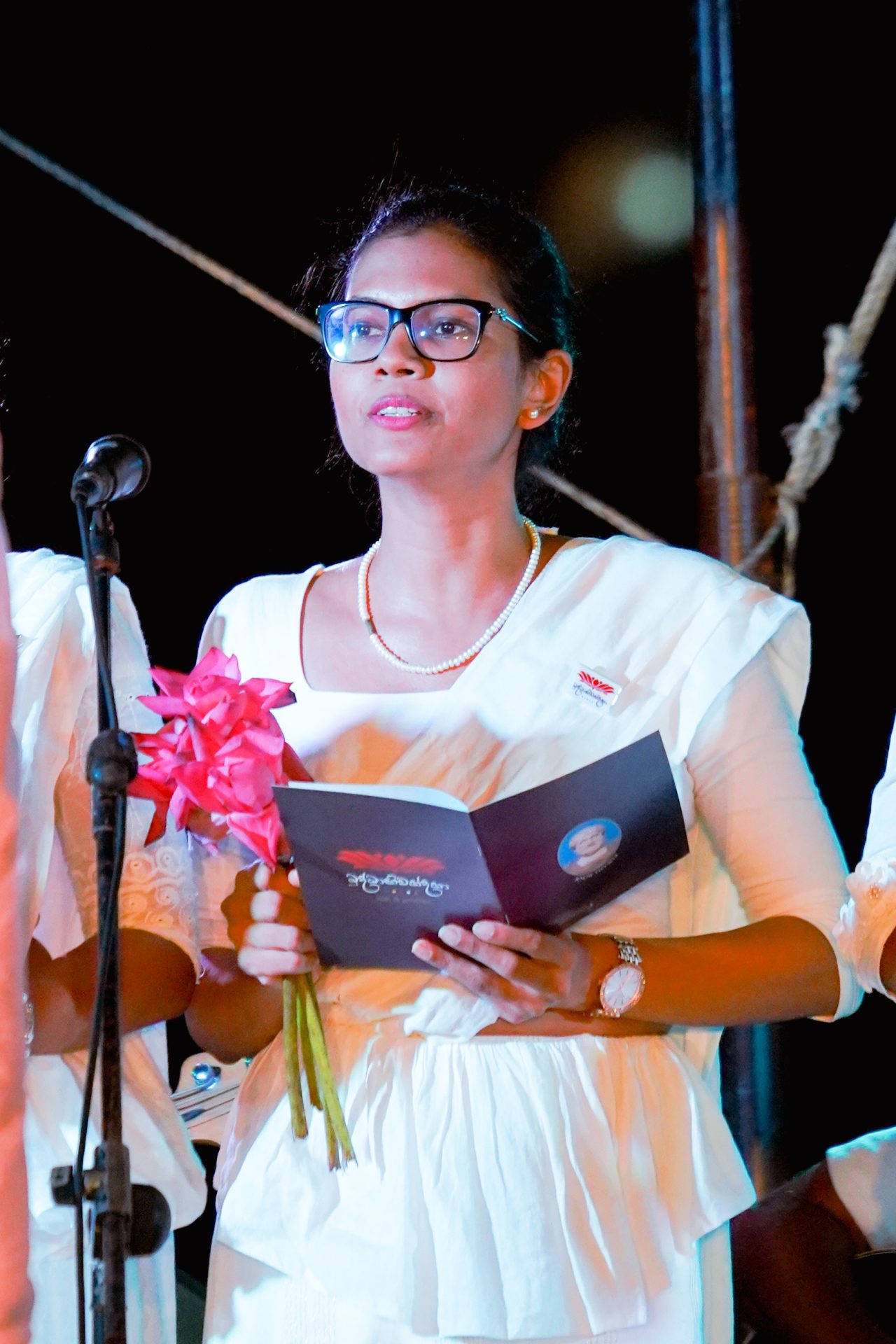 Young woman in white outfit speaking at formal event.