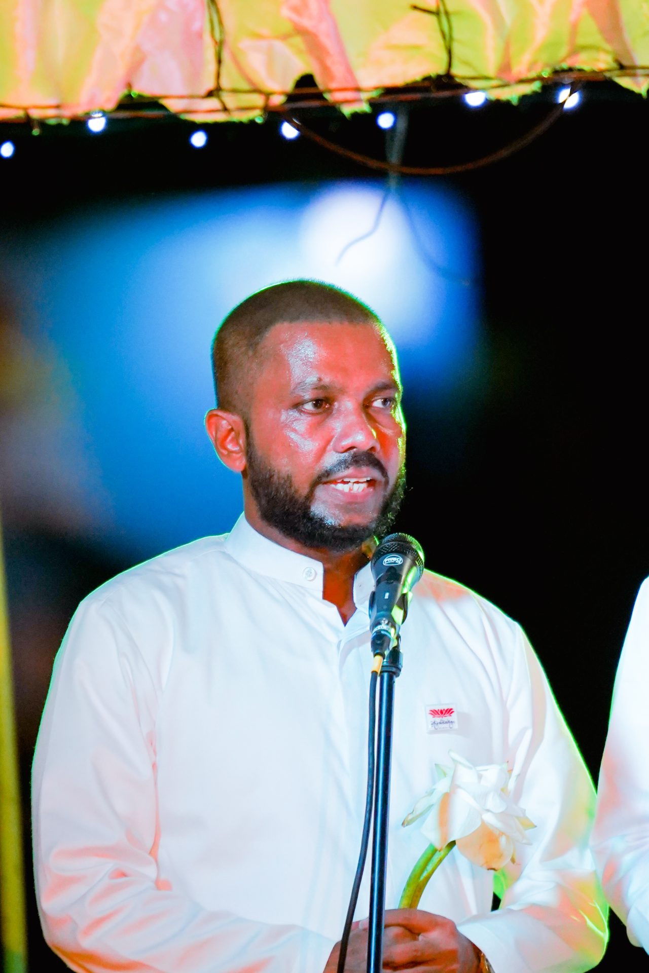 Man in traditional attire speaking at a solemn cultural event.