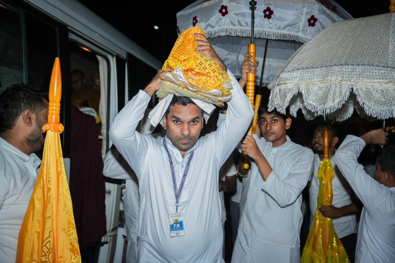 Cultural procession at night with traditional attire, ceremonial fabrics, ornate umbrellas, and a bus.