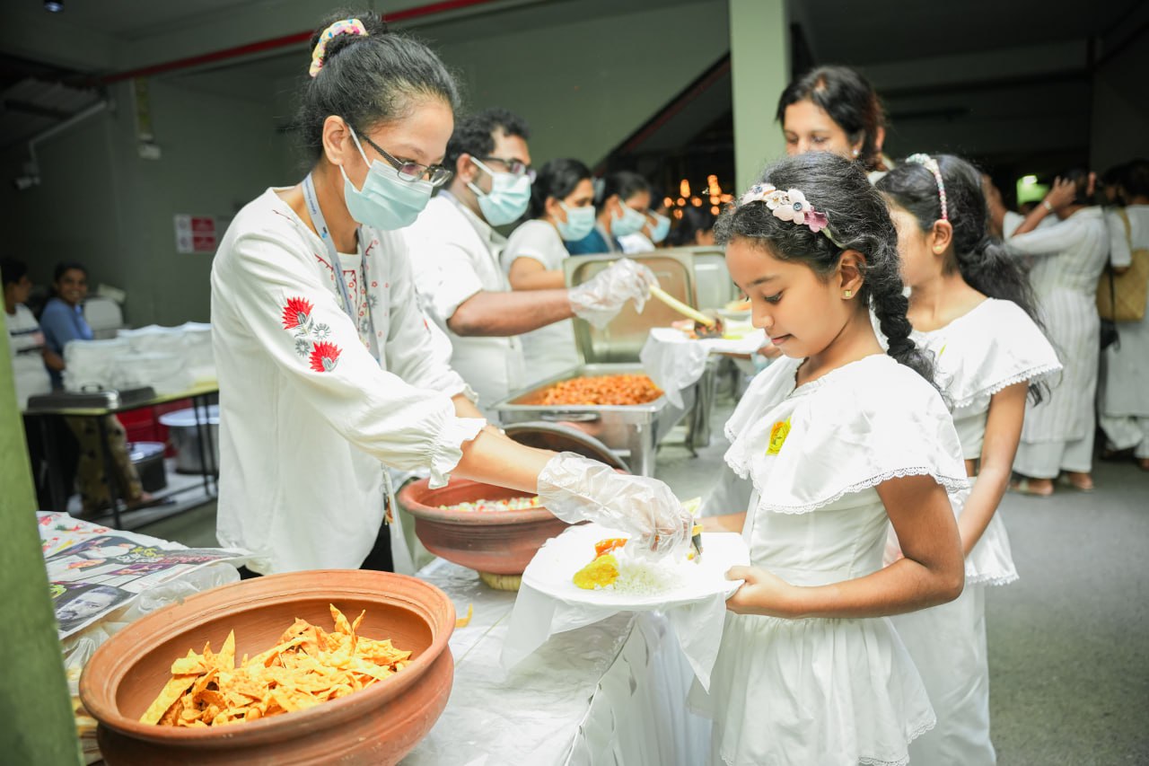 Communal meal event with volunteers serving food to children, everyone wearing face masks.