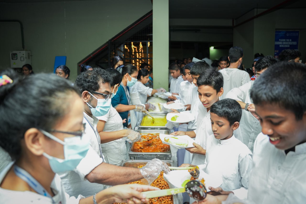 Community meal distribution with volunteers serving food to children in a lively hall.