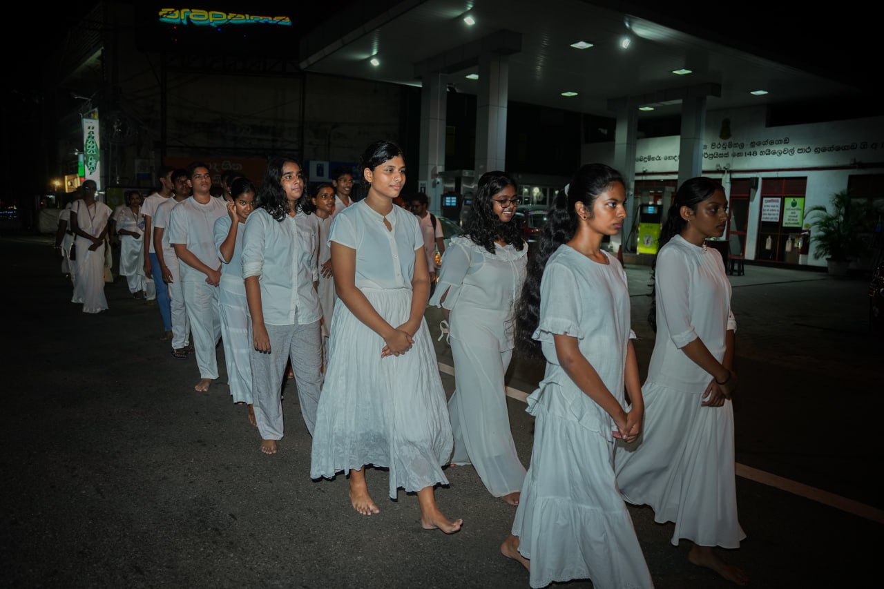 Solemn nighttime procession near urban gas station.