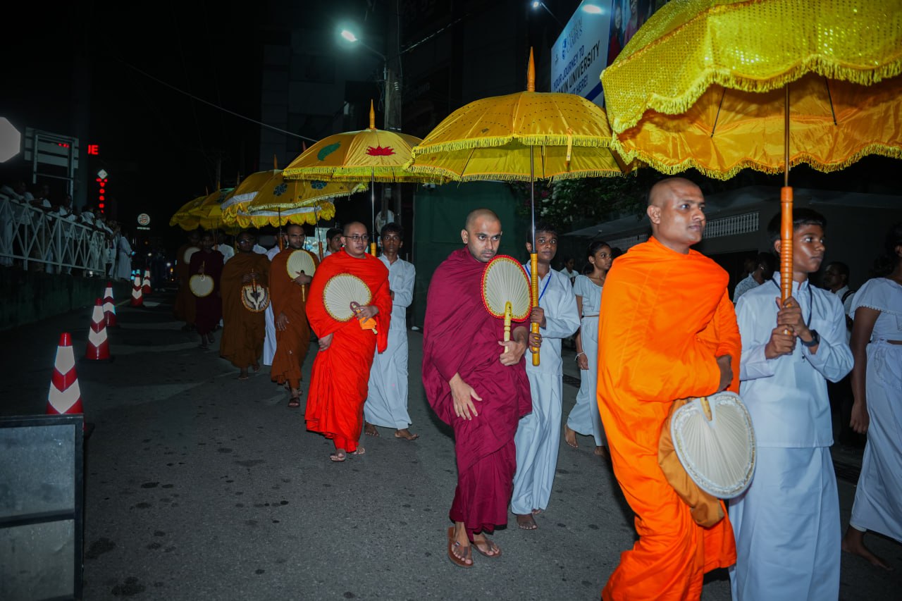 Buddhist monks nighttime street procession with ornate fans and parasols in urban setting.