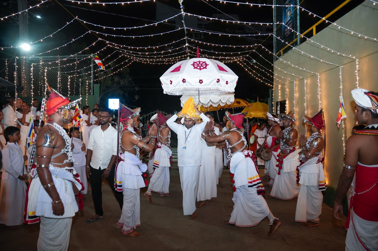 Traditional festival performers in ornate costumes under festive lights during a night ceremony.