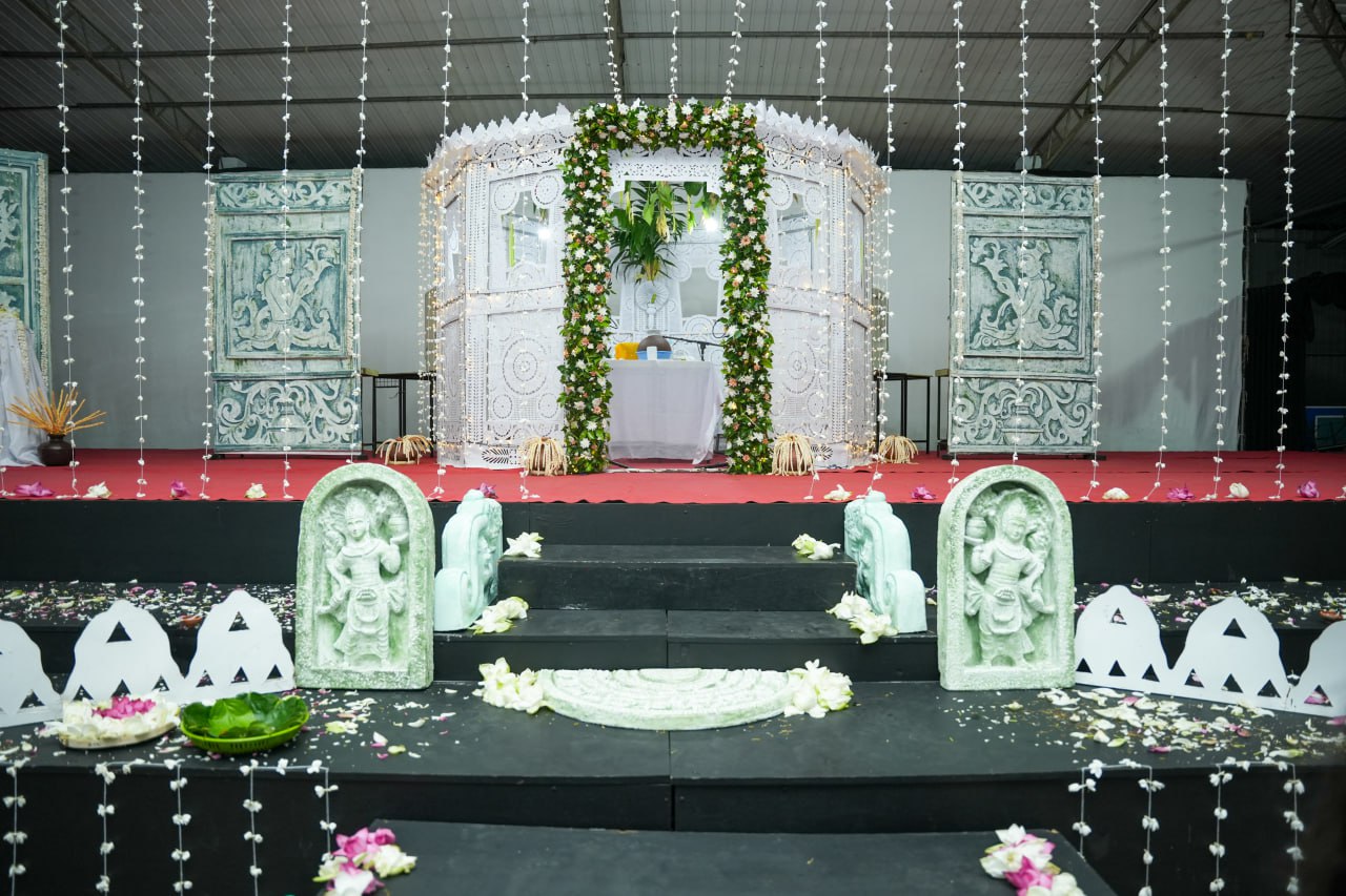 Elaborately decorated stage with flowers, statues, red carpet, and gazebo for a ceremonial event.