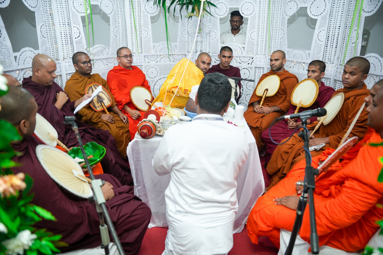 Monks in traditional robes perform a solemn Buddhist ritual around a ceremonial table.