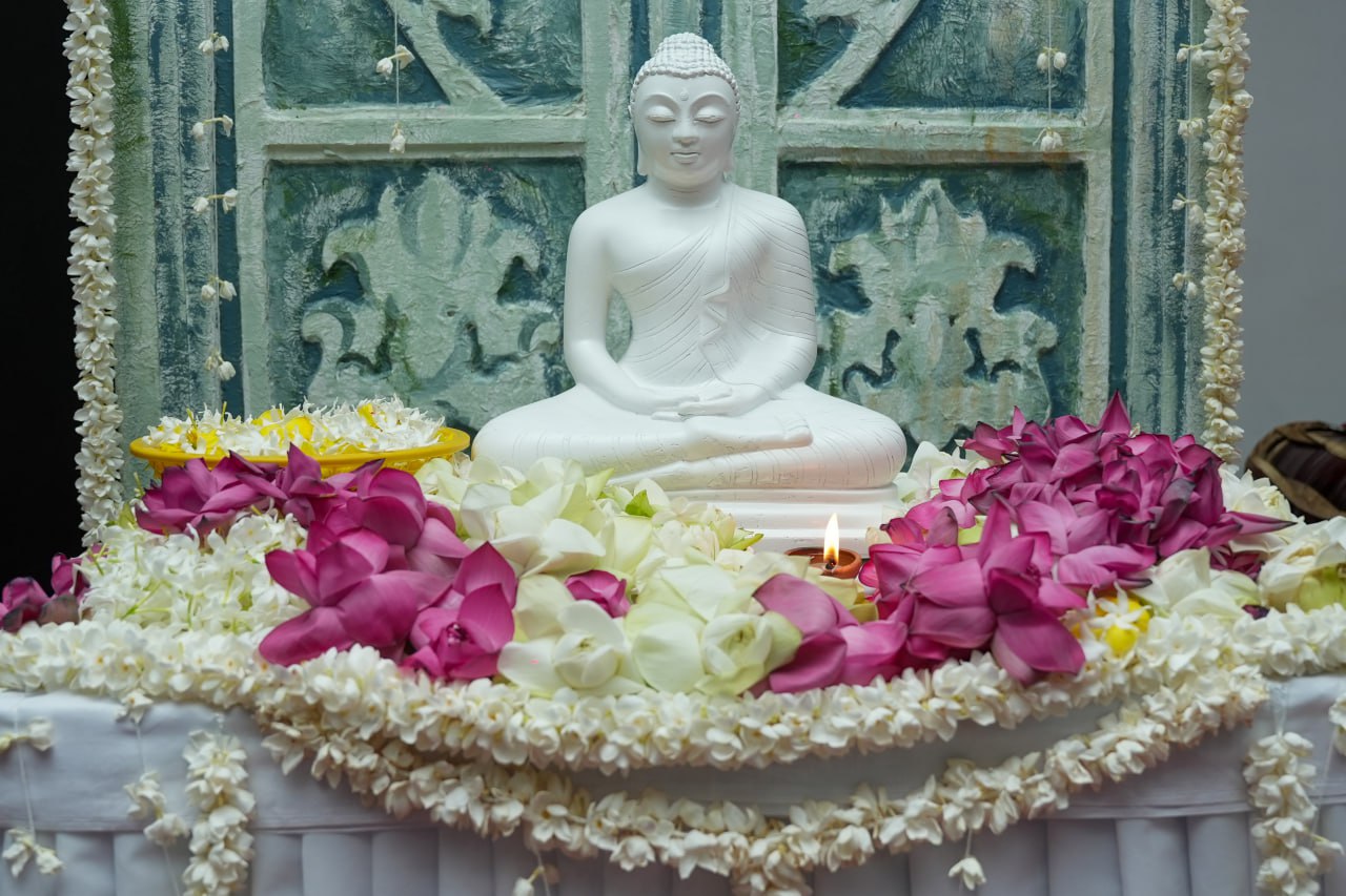 Buddha statue with lotus flowers and candle on a decorated altar.