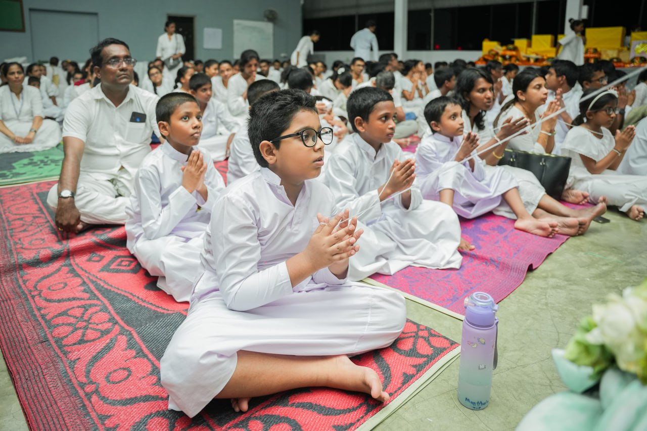 Children in white attire meditating in a communal prayer session.
