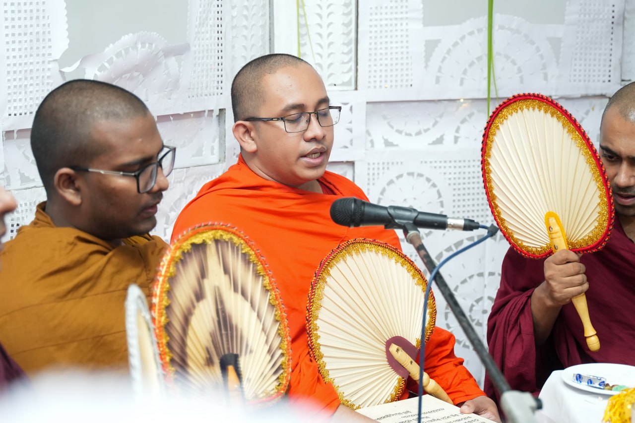 Buddhist monks in ceremonial attire performing ritual with decorative fans and microphones.