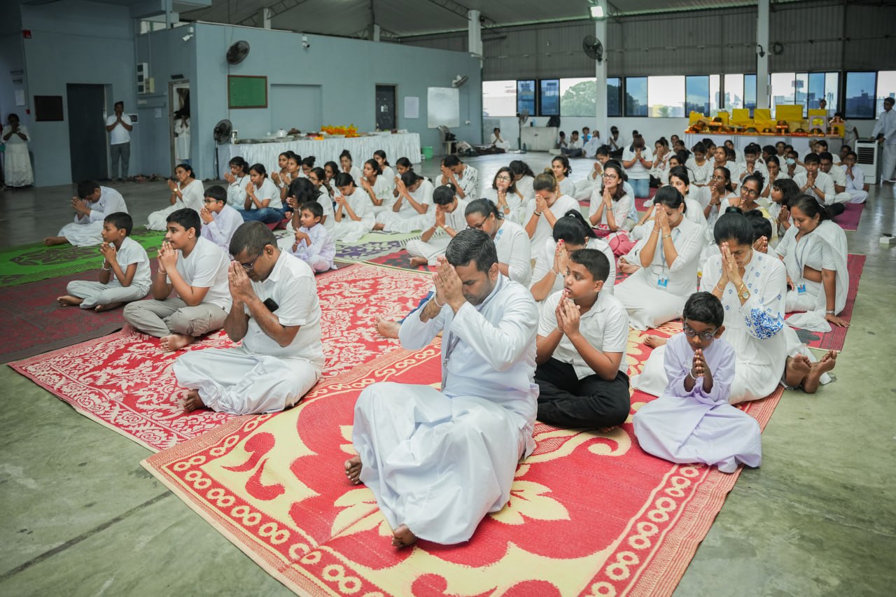 Large indoor prayer gathering with adults and children in white clothing.