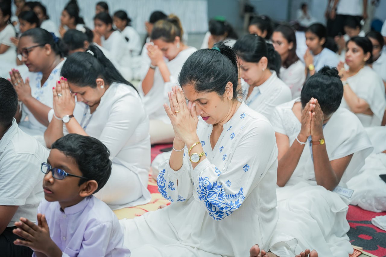 Group prayer meditation session with diverse participants in white attire.
