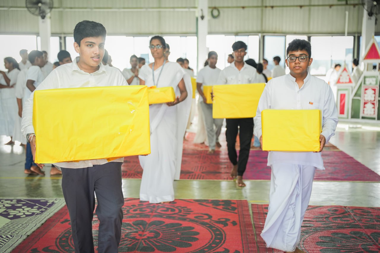 Ceremonial procession with participants in white carrying yellow boxes in a decorated hall.
