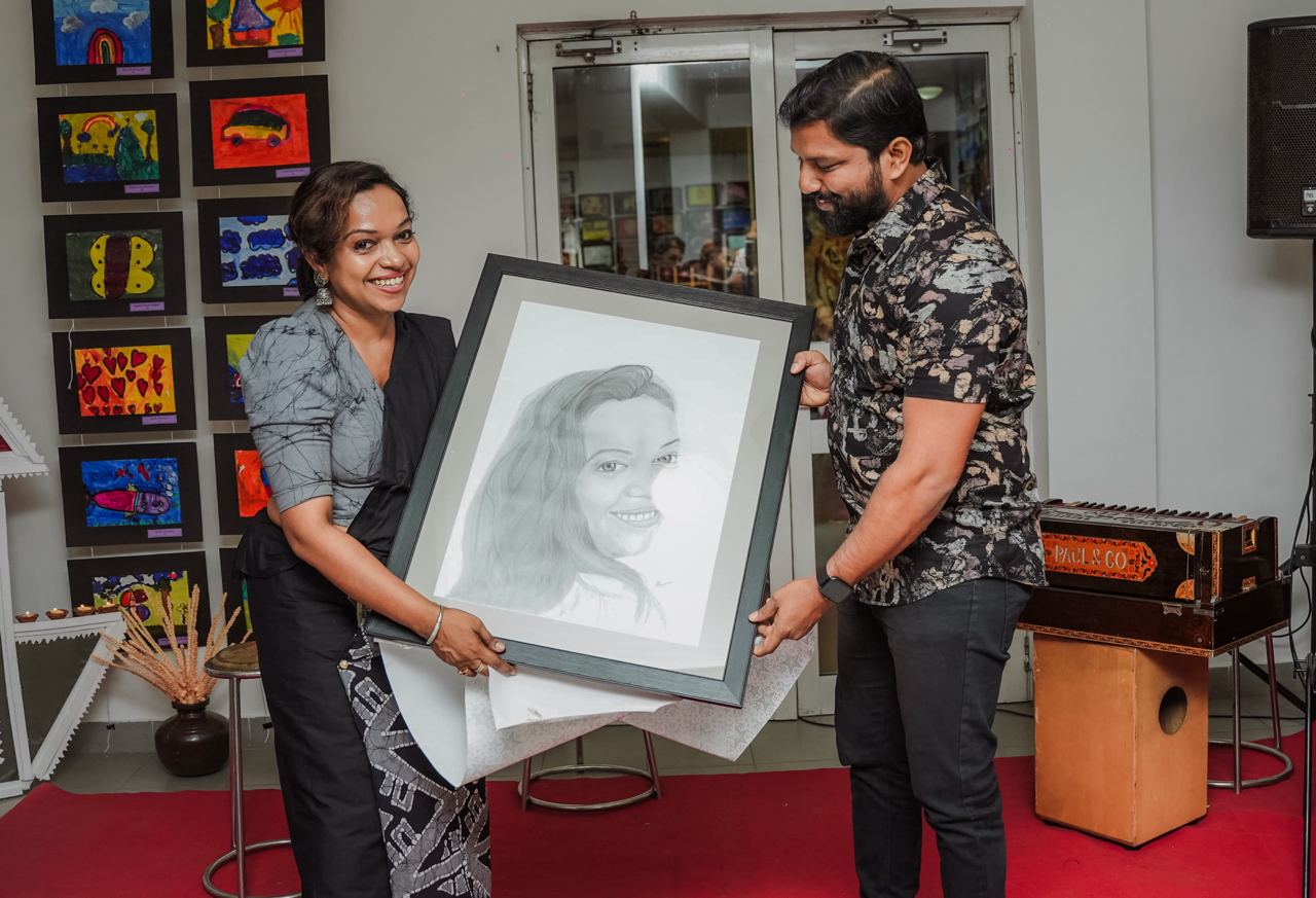 Celebratory Portrait Presentation at Art Gallery Art gallery exhibit: two people presenting a framed portrait amidst colorful childrens artwork.