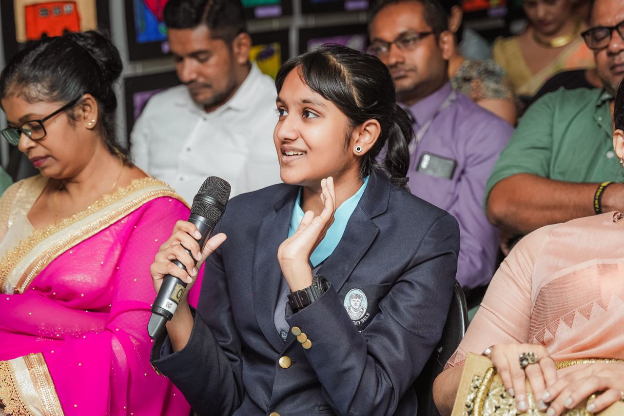 Engaged Seminar Attendee Asking Question Young woman in blazer asking question at seminar, vibrant attendees in background.