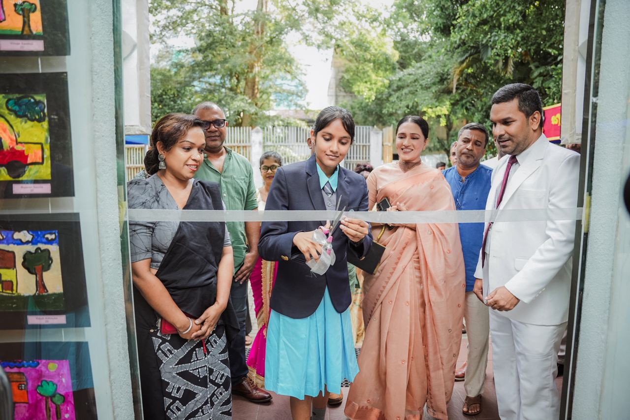 School Art Exhibition Inauguration Ribbon Cutting Ceremony Young girl cutting ribbon at school event, surrounded by smiling adults.