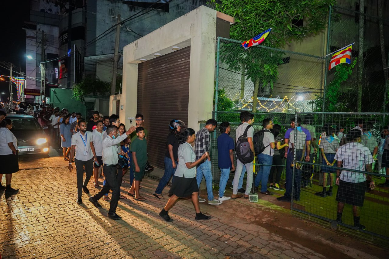 Community Gathering at Festive Event with Colorful Flags Lively evening queue outside festive venue with flags, families, and twinkling lights.