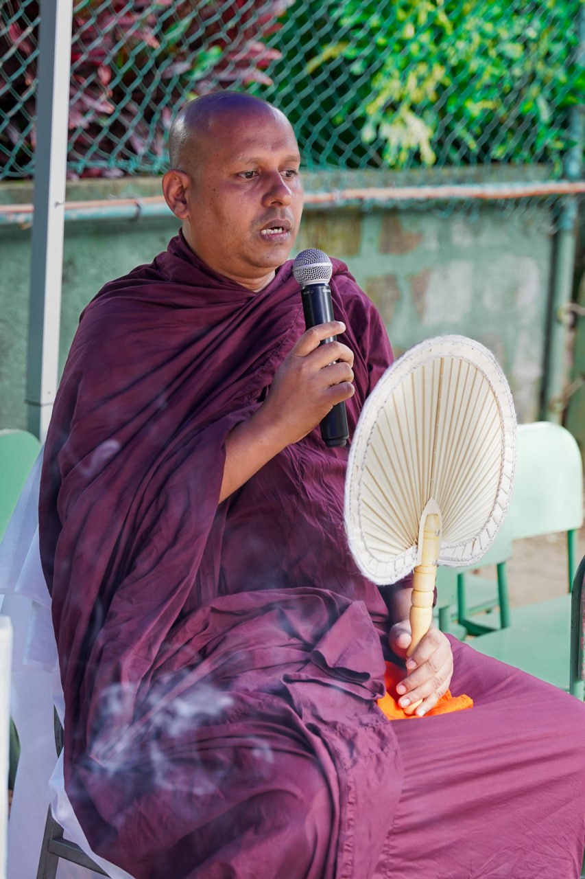 Tranquil Outdoor Lecture by Buddhist Monk with Traditional Fan Buddhist monk in maroon robe giving a serene outdoor lecture holding a traditional fan.