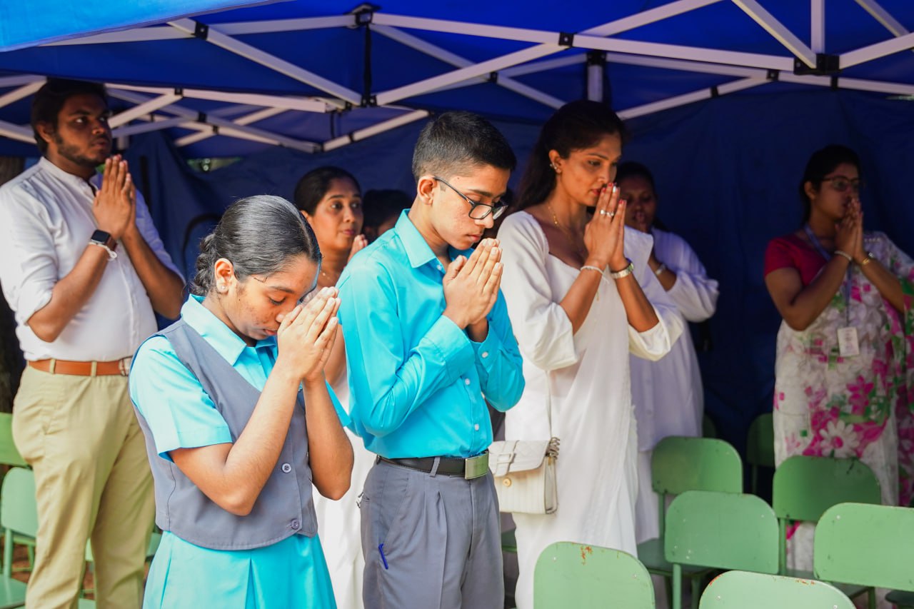 Solemn Community Prayer Ceremony Under Blue Tent Community prayer gathering under blue tent with children and adults in solemn reflection.