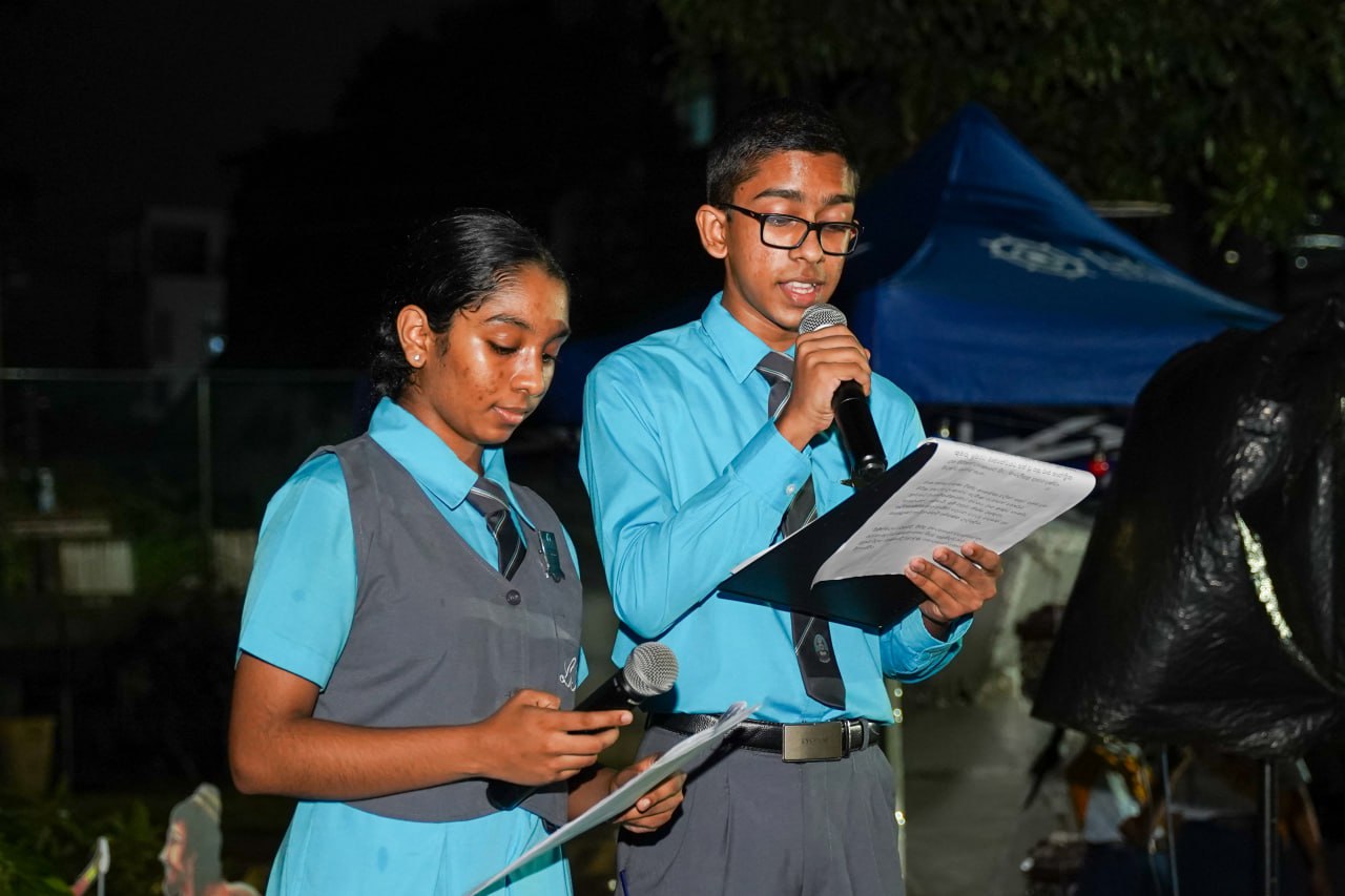 Evening School Event: Students Delivering Speeches Two students delivering speeches at an outdoor evening school event under a blue canopy.