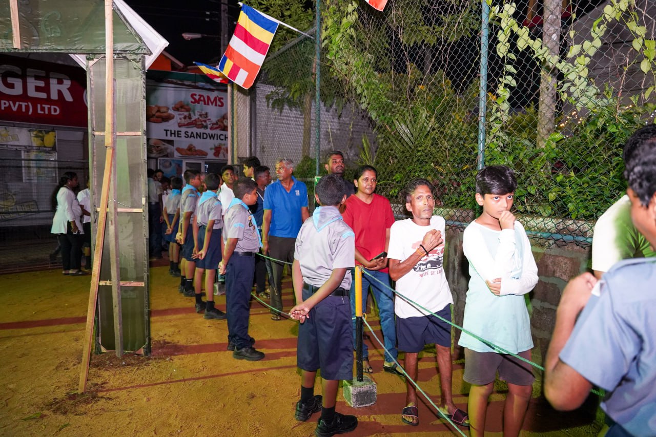 Children Queuing at Evening Community Event Children in uniforms queue at an evening event under festive flags and artificial lights.