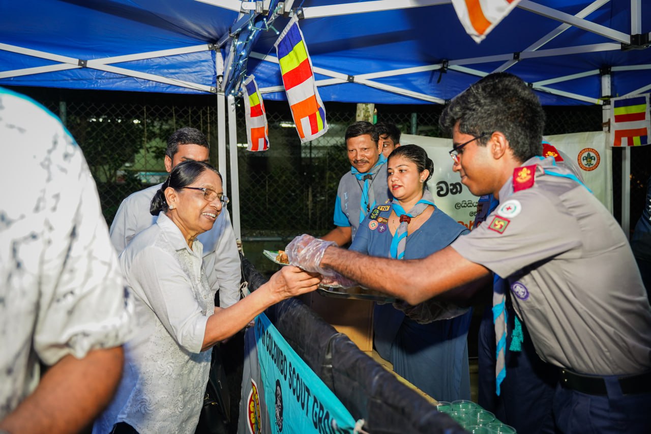 Community Unity: Scouts Serving Smiles Under Blue Canopy Scouts serving community under blue canopy with flags, fostering unity and joy.