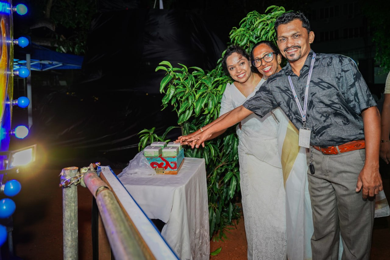 Joyful Cake Cutting Celebration with Friends and Festive Lights Friends celebrating with cake, smiling, colorful lights, lush greenery, and festive attire.
