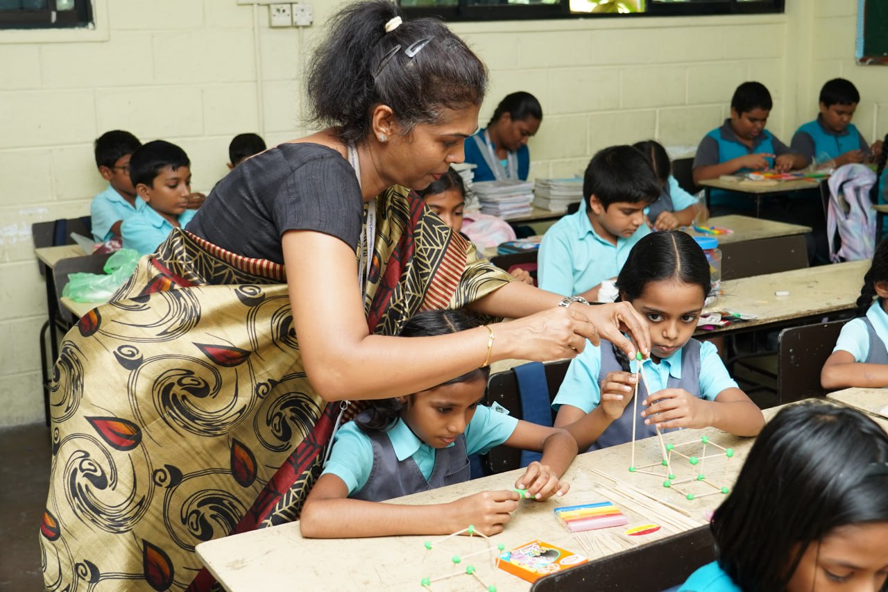 Engaging Classroom: Teacher Assists with 3D Geometry Project Teacher assists students with 3D geometry project in a bright, interactive classroom.