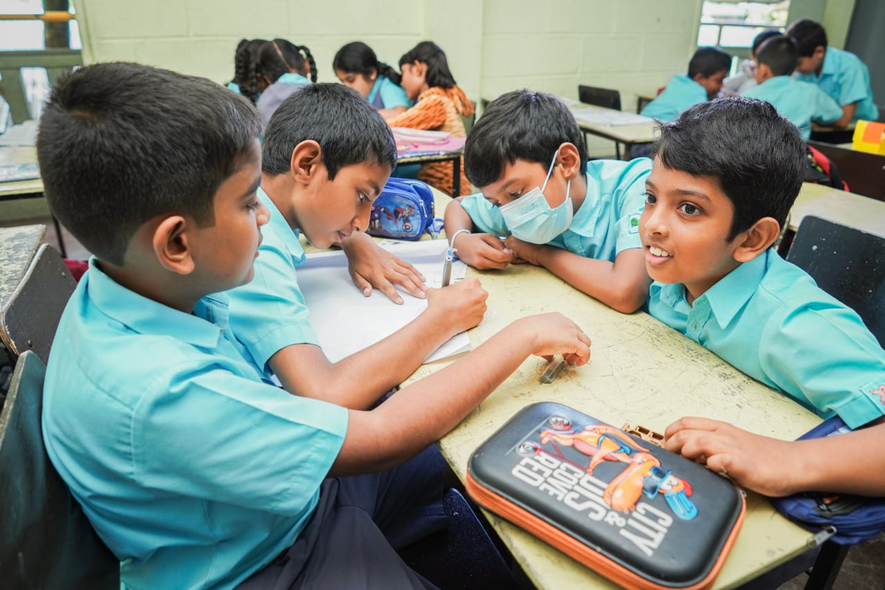 Collaborative Learning in a Bright Classroom Young students collaborating on a classroom project, with one wearing a face mask.