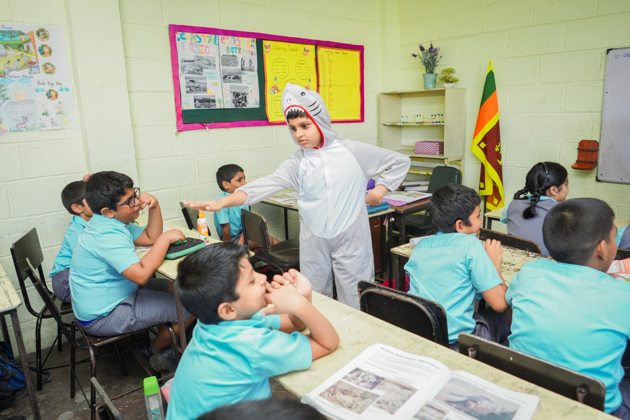 Interactive Learning in a Sri Lankan Primary Classroom Sri Lankan classroom with students in uniforms; one child in a shark costume presenting.