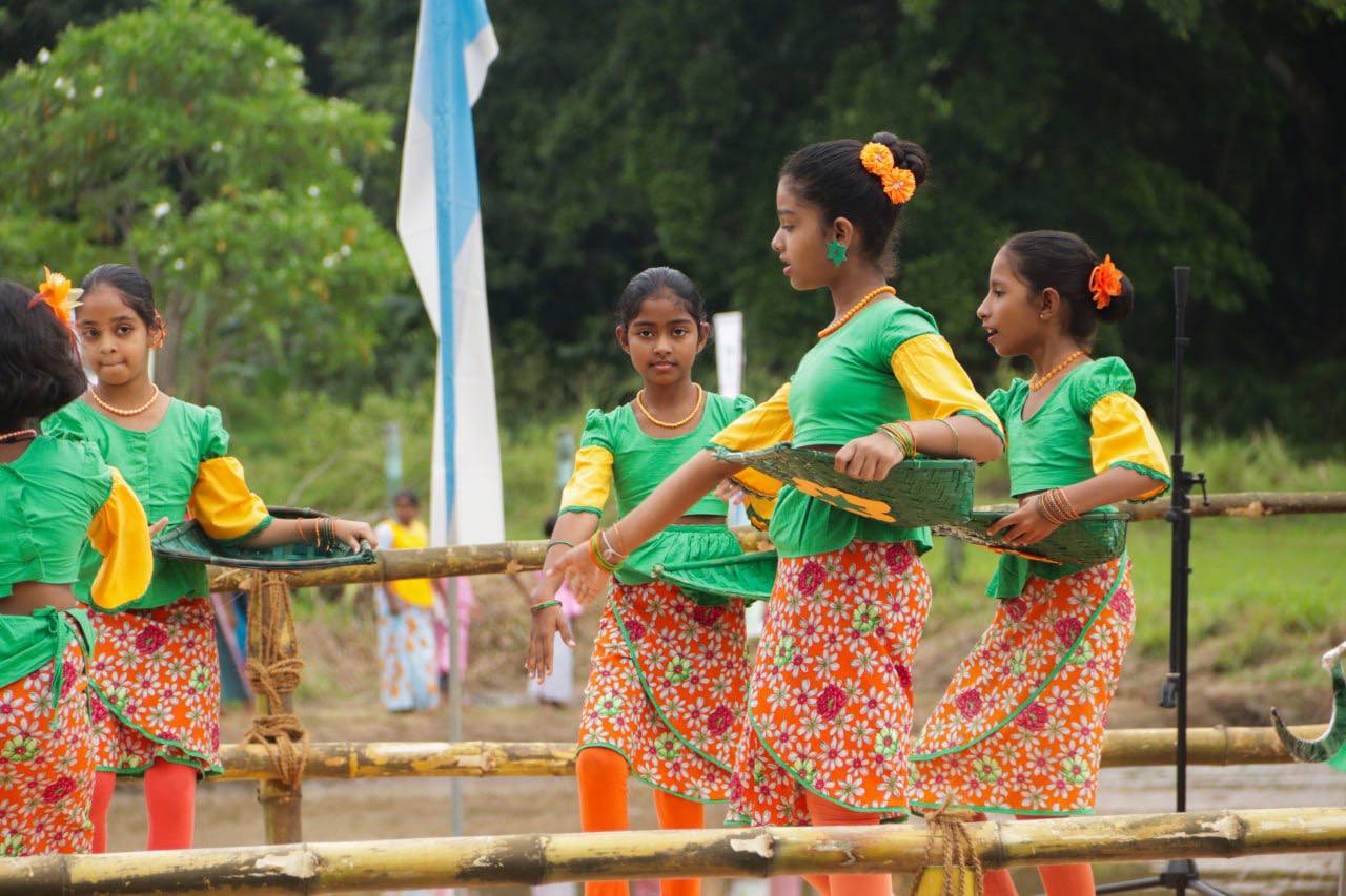 Young girls in colorful traditional outfits performing a cultural dance amid lush greenery.