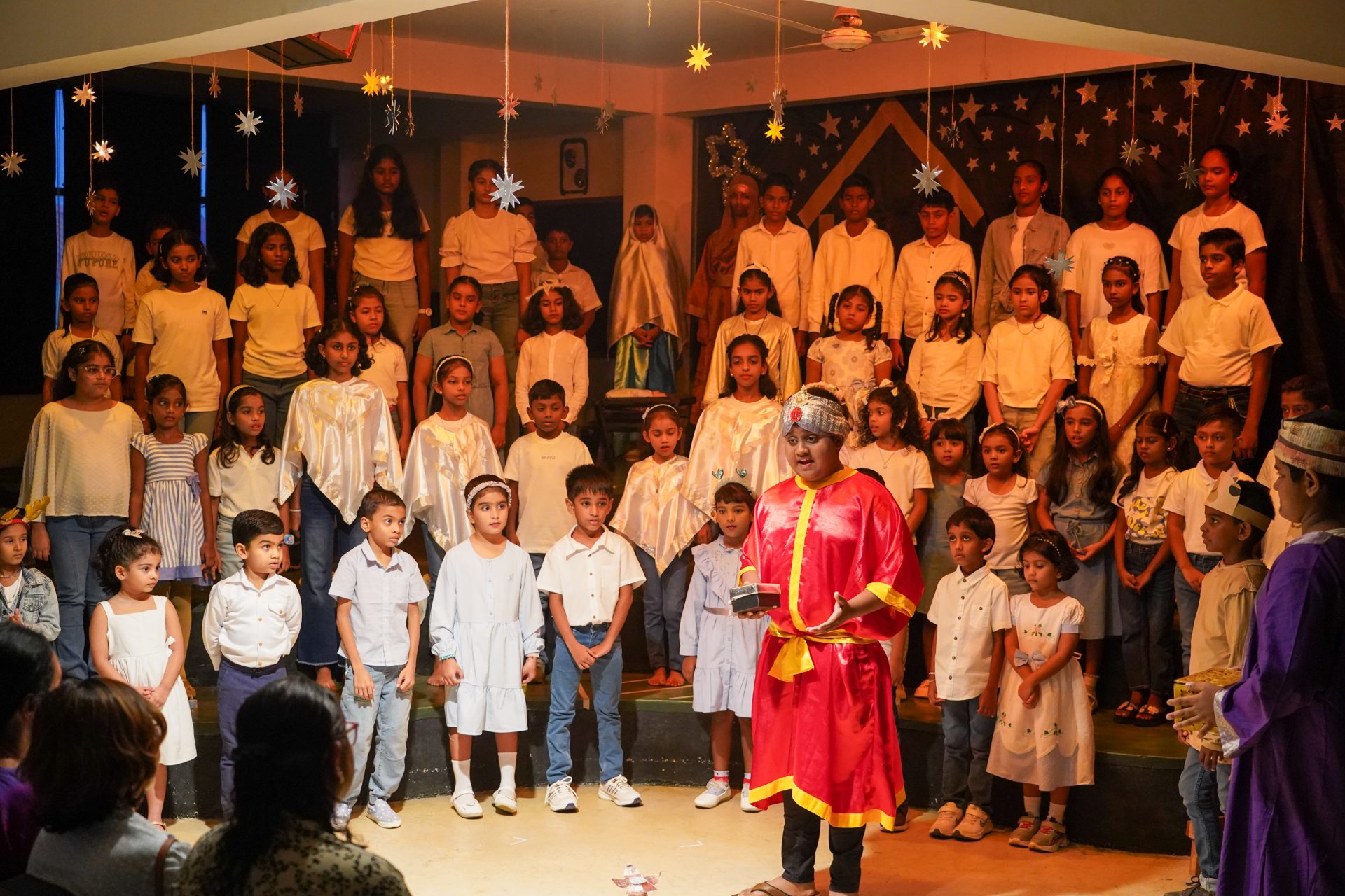 Childrens starry night performance with colorful costumes on a festive stage, engaging captivated audience.