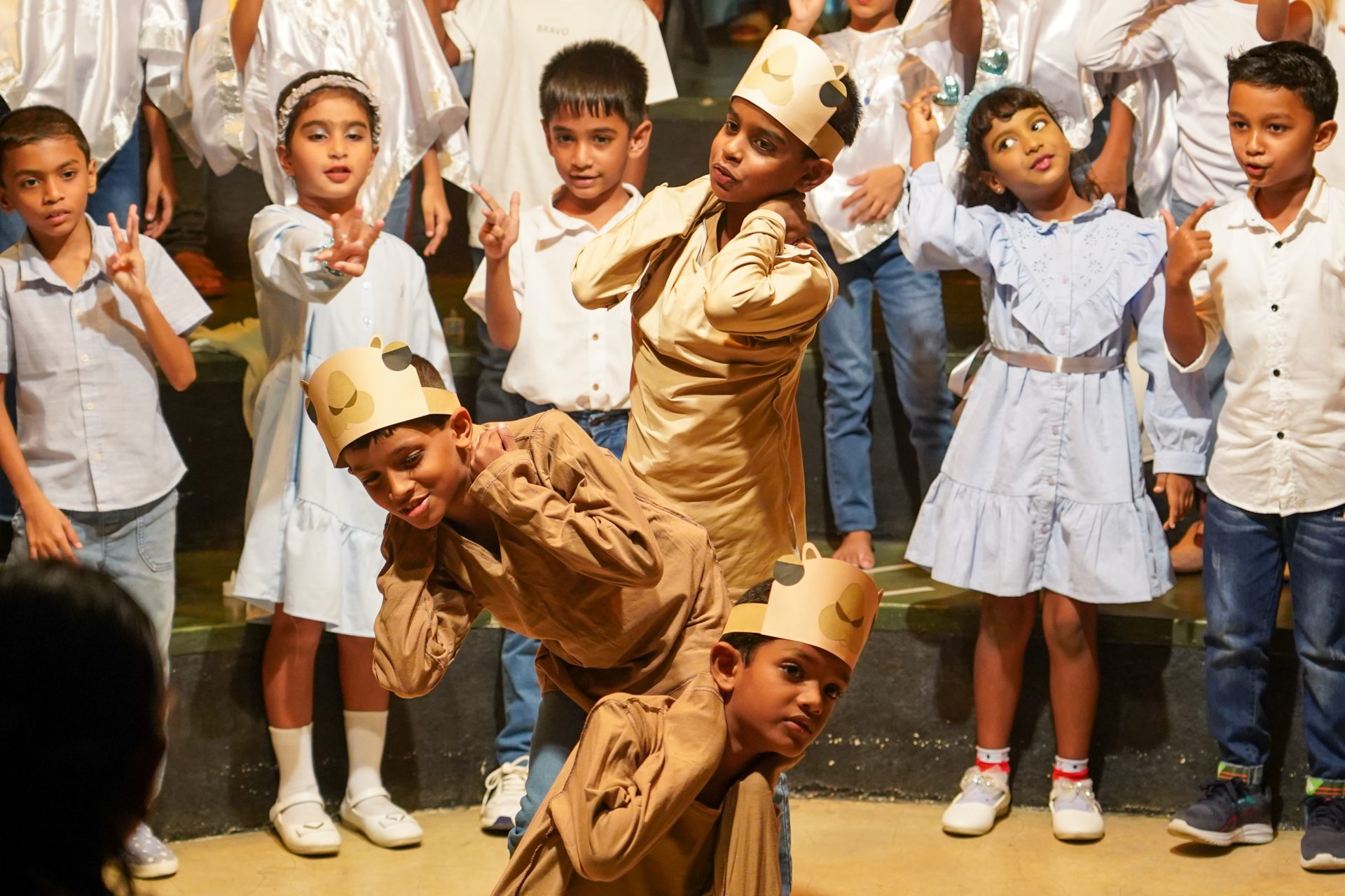 Children in costumes perform a joyful school play with choir support.
