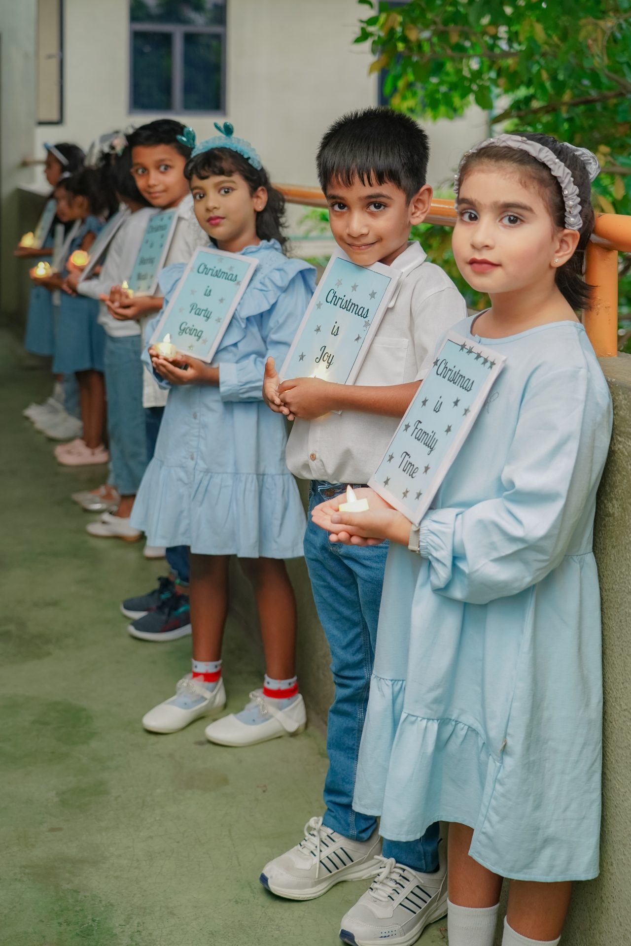 Children in blue read open books, diverse group in school hallway.